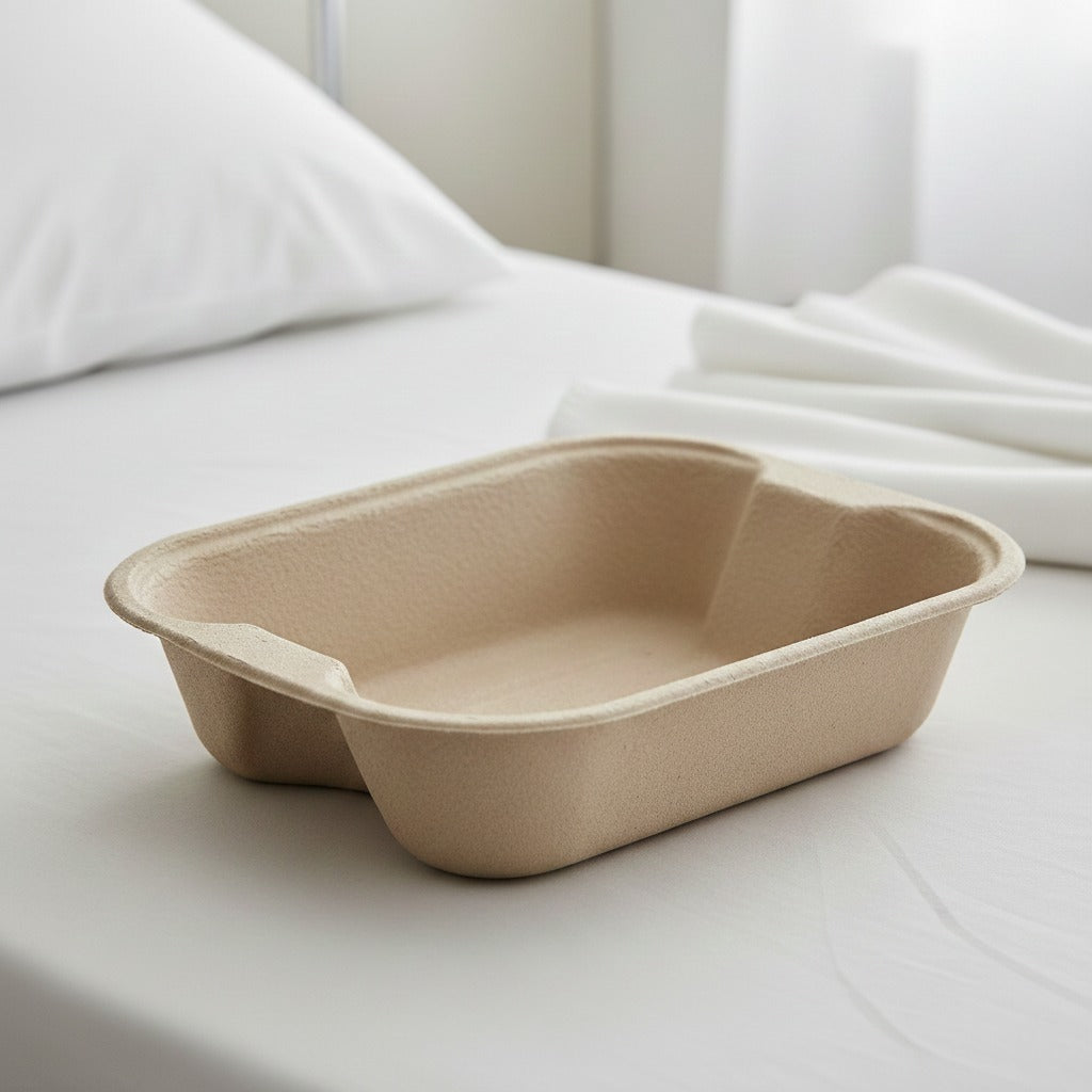 Beige disposable molded pulp bedpan tray on a hospital bed, eco friendly plastic free biodegradable medical packaging for patient care